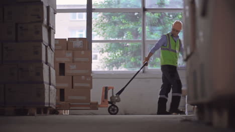 worker in helmet and yellow vest pulling a forklift loaded with boxes