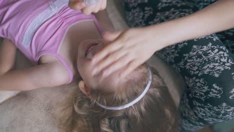 mommy gives eyes drops to smiling girl lying on large bed