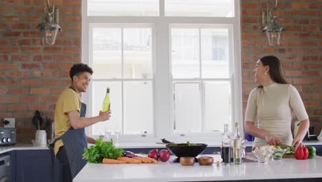 Happy-biracial-couple-cooking-together-and-drinking-wine-in-kitchen