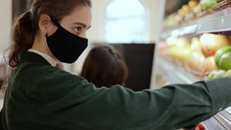 two women choosing bio fruits in supermarket together, wearing mask