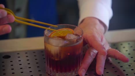 Cocktail-bartender-prepares-a-martini-with-a-dehydrated-orange-slice-and-ice