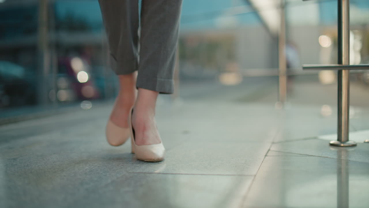 Leg view of lady walking in nude color heels beside glass reflecting surroundings and urban background, with soft lighting and smooth stride, conveying confidence