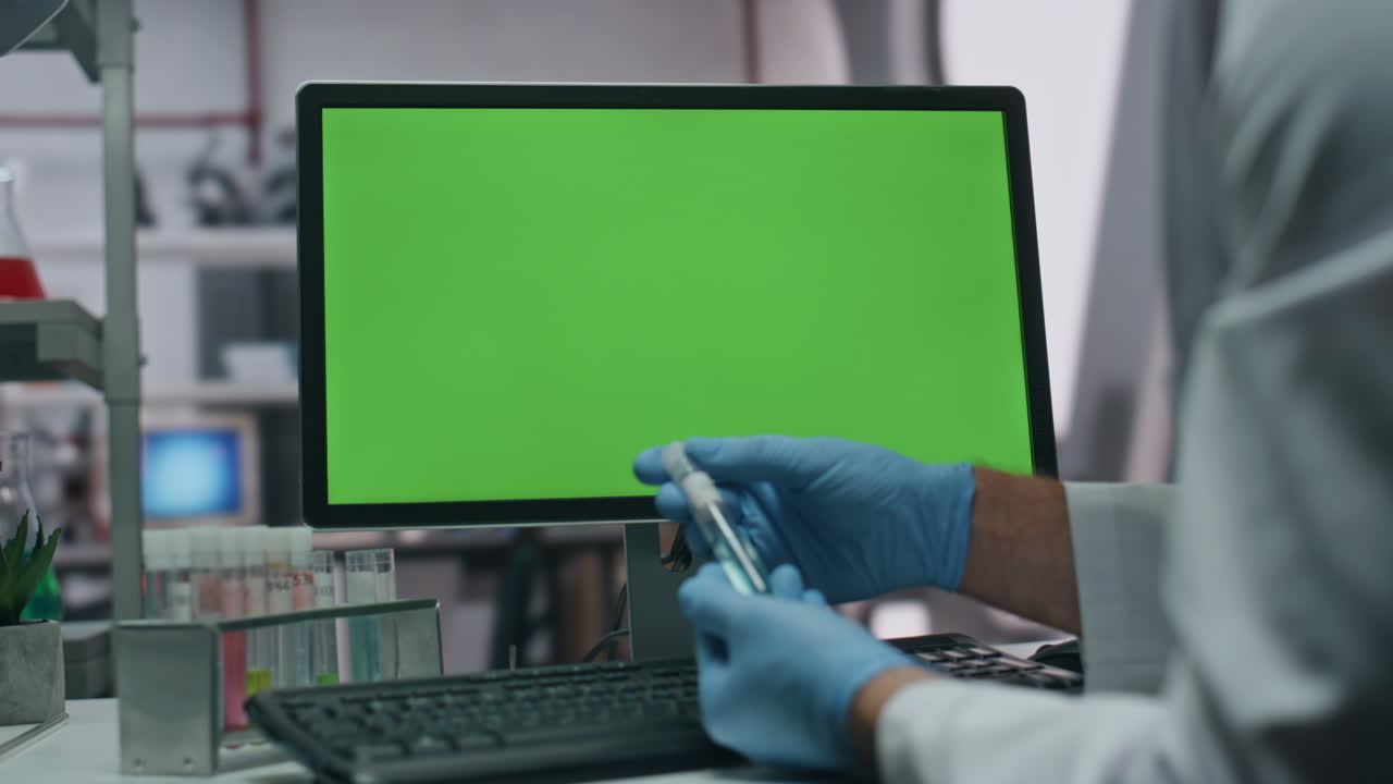 guantes tomando tubo de ensayo ingresando datos de investigación en la computadora de pantalla verde