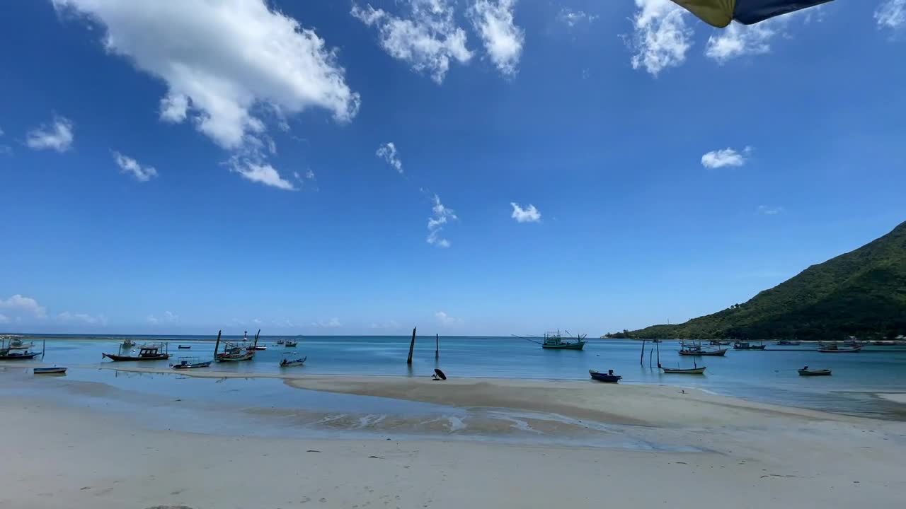 A tranquil beach scene in Thailand featuring boats gently floating on crystal clear waters, under a bright, clear sky. Golden sands meet azure seas in this idyllic coastal setting