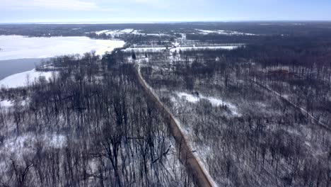 Drone-Retrocediendo-Sobre-Un-Bosque-En-Invierno-Siguiendo-A-Un-Camión-En-La-Carretera