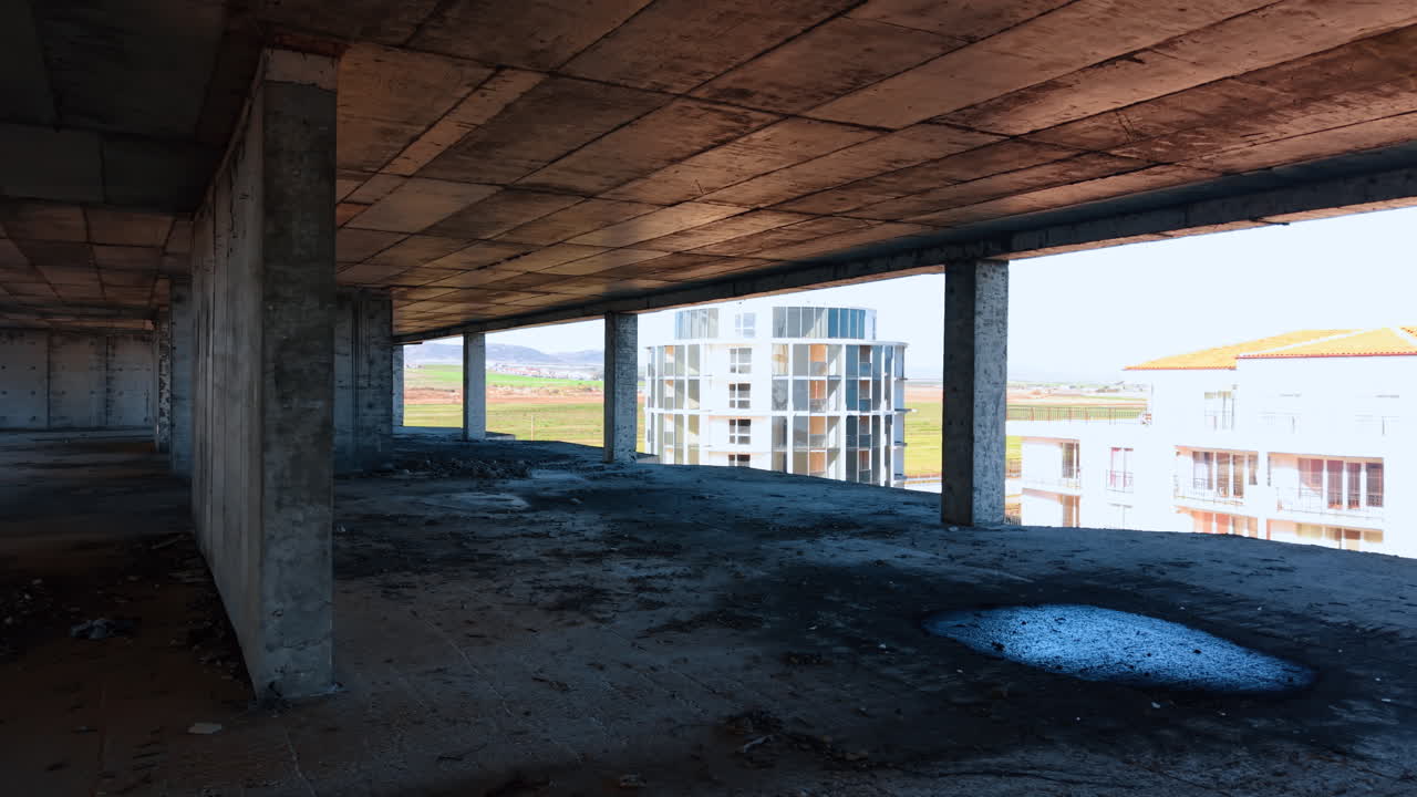 View from inside concrete construction site of modern building. Wide angle interior shot of an unfinished building floor with concrete pillars and a view of a nearby house