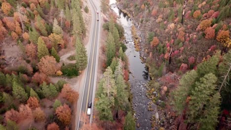 Esta-Toma-Aérea-Muestra-Autos-Bajando-Por-La-Carretera-Junto-A-Un-Río-Que-Fluye-Durante-El-Otoño