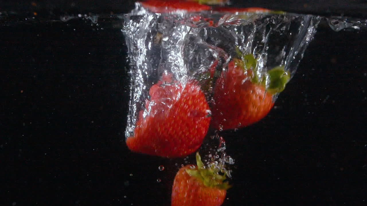 Movimento rallentato: molte fragole fresche e belle cadono in acqua con bolle