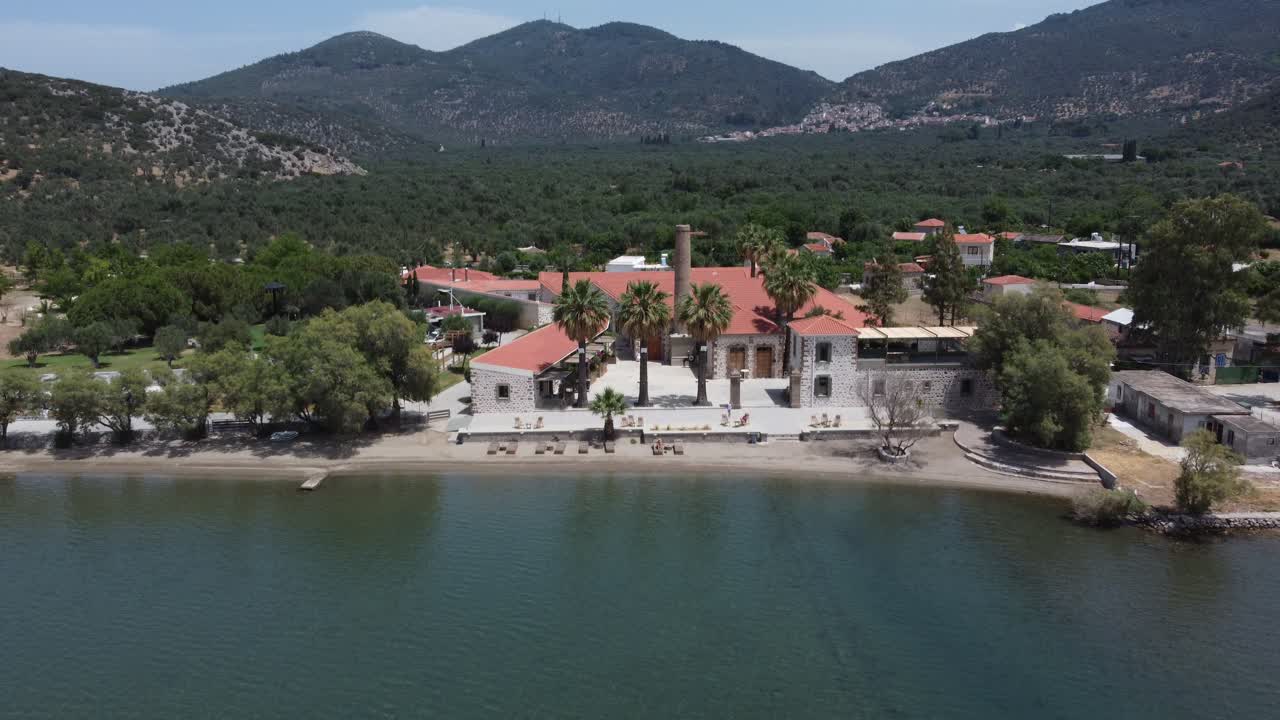 A luxury yacht sailing at seaport with Zaira hotel estate in background surrounded with olive trees garden landscape and mountains, Mytilene, Lesvos Island, Aerial view