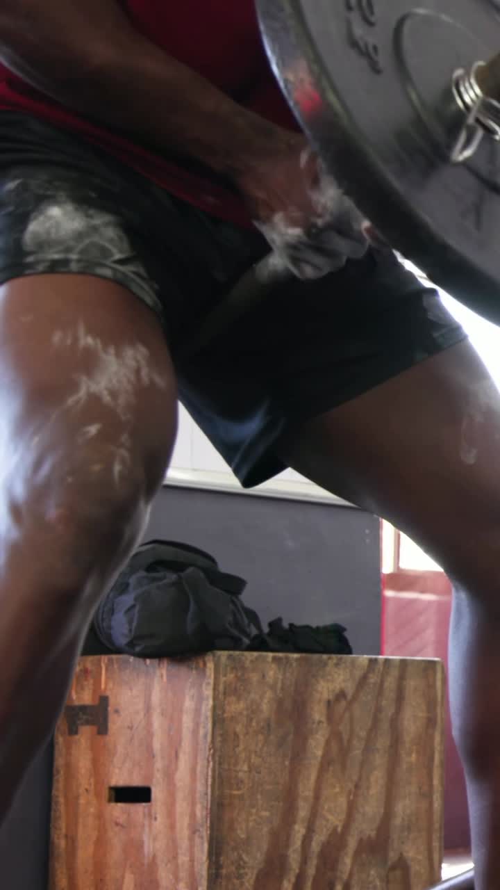 Vertical video: Adjusting grip, man in red shirt, dark shorts pulling barbell rows at gym for power