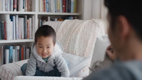 funny little asian boy jumping onto sofa playing with father happy dad enjoying playful game with son at home 4k