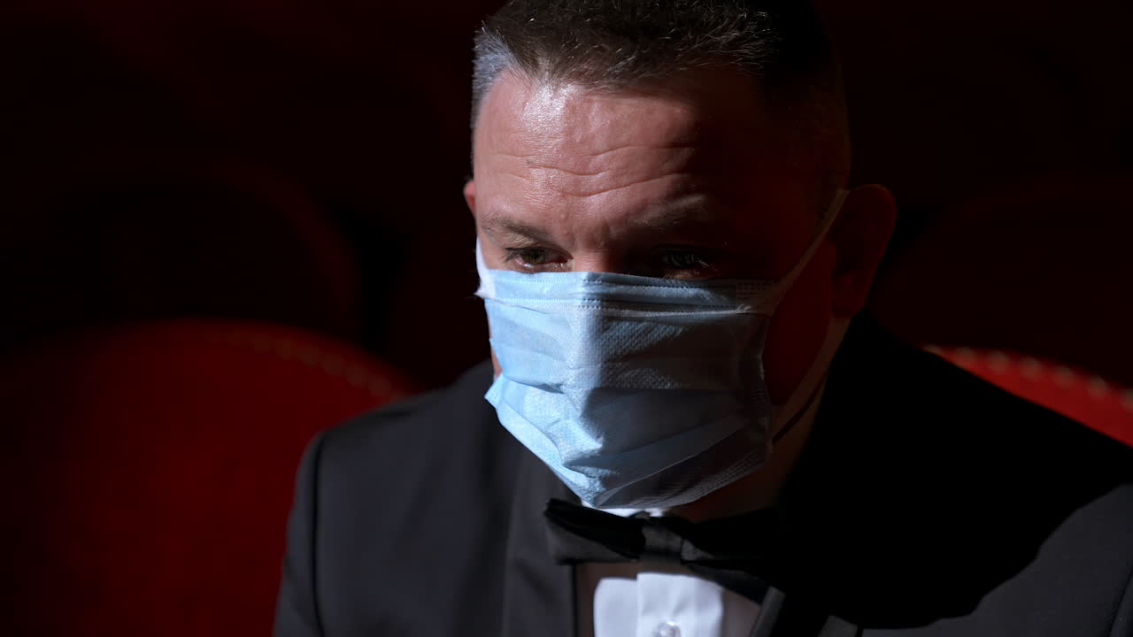 Lonely and sad visitor sits in empty theater hall alone. Person sits on a red chair during pandemic.