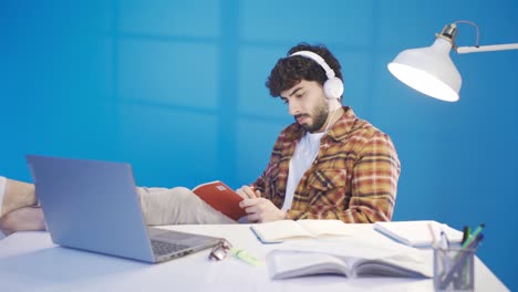 joven despreocupado y relajado estudiando con los pies en la mesa, escuchando música con auriculares.