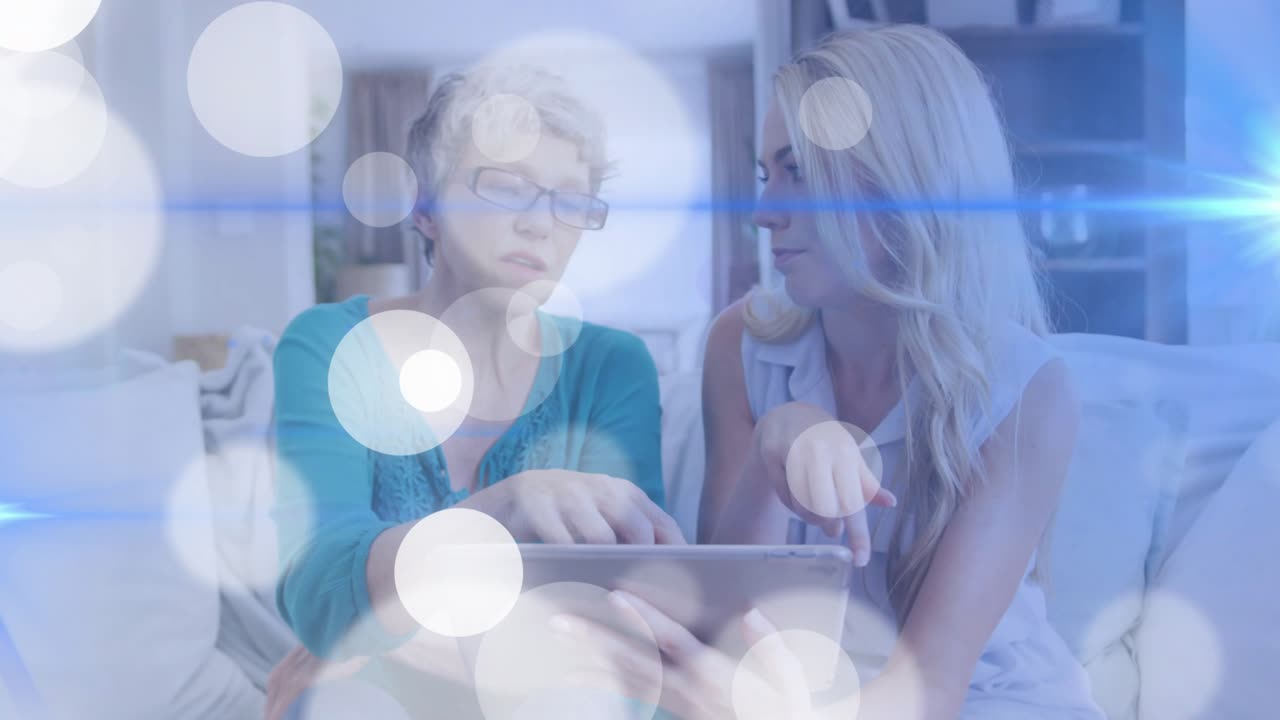 Donna anziana che tocca un tablet e una donna adulta che la guida nei passaggi tecnologici, tra un bokeh con bagliori blu.