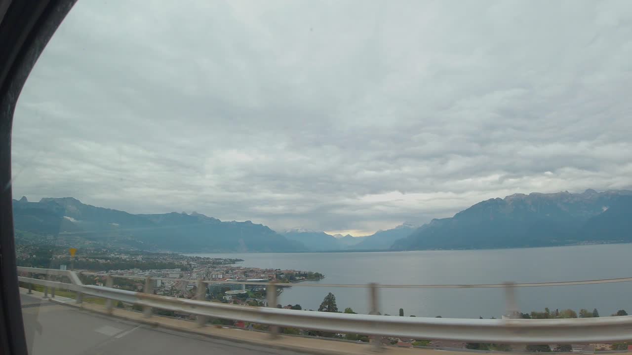 A view of a beautiful town underneath the motorway adjacent the sea and landscape view of mountains series, in a cloudy weather, from the car window