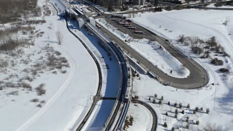 Ottawa-LRT-Train,-Winter-Snow,-Wide-Aerial-Shot-Following-Train,-Ottawa,-Canada