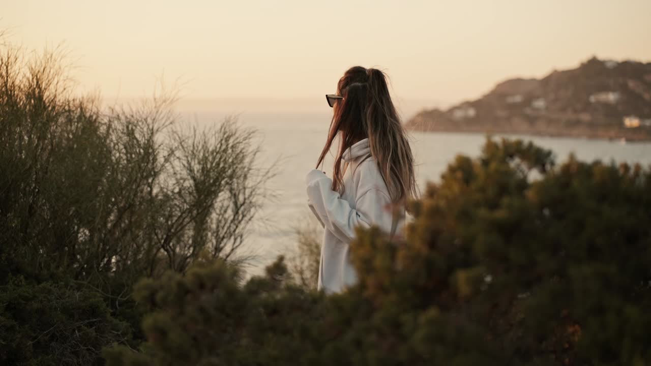 Slow motion shot of a woman playing with her hair and watching the sunset