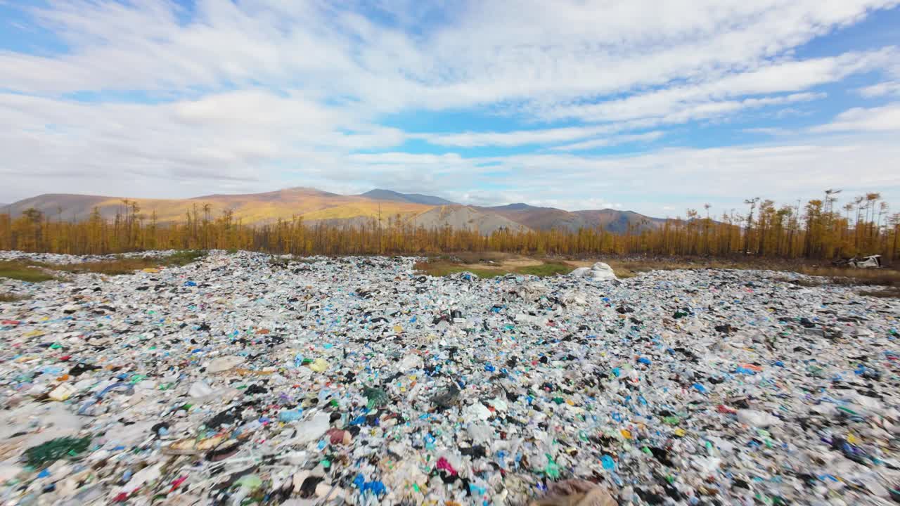 A vast landscape unfolds, showcasing a remote household waste dump surrounded by vibrant autumn foliage and distant mountains. Nature contrasts sharply with this human impact on the environment.