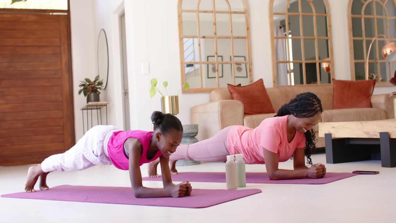Mother and child in pink gear practicing forearm plank on purple mats at home, mother showing