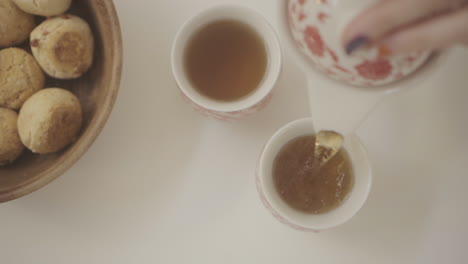 top view of a person pouring tea into cups while a bowl of freshly baked chipa bread sits on the table, creating a cozy home traditional atmosphere