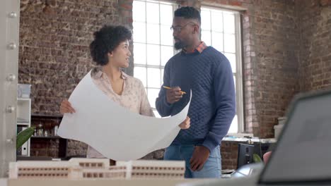 Diverse-architect-colleagues-discussing-work-with-building-model-and-blueprints-in-slow-motion