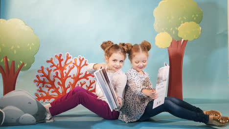 two little girls reading a book on a blue background. friends. childhood. friendship. fairy tales.