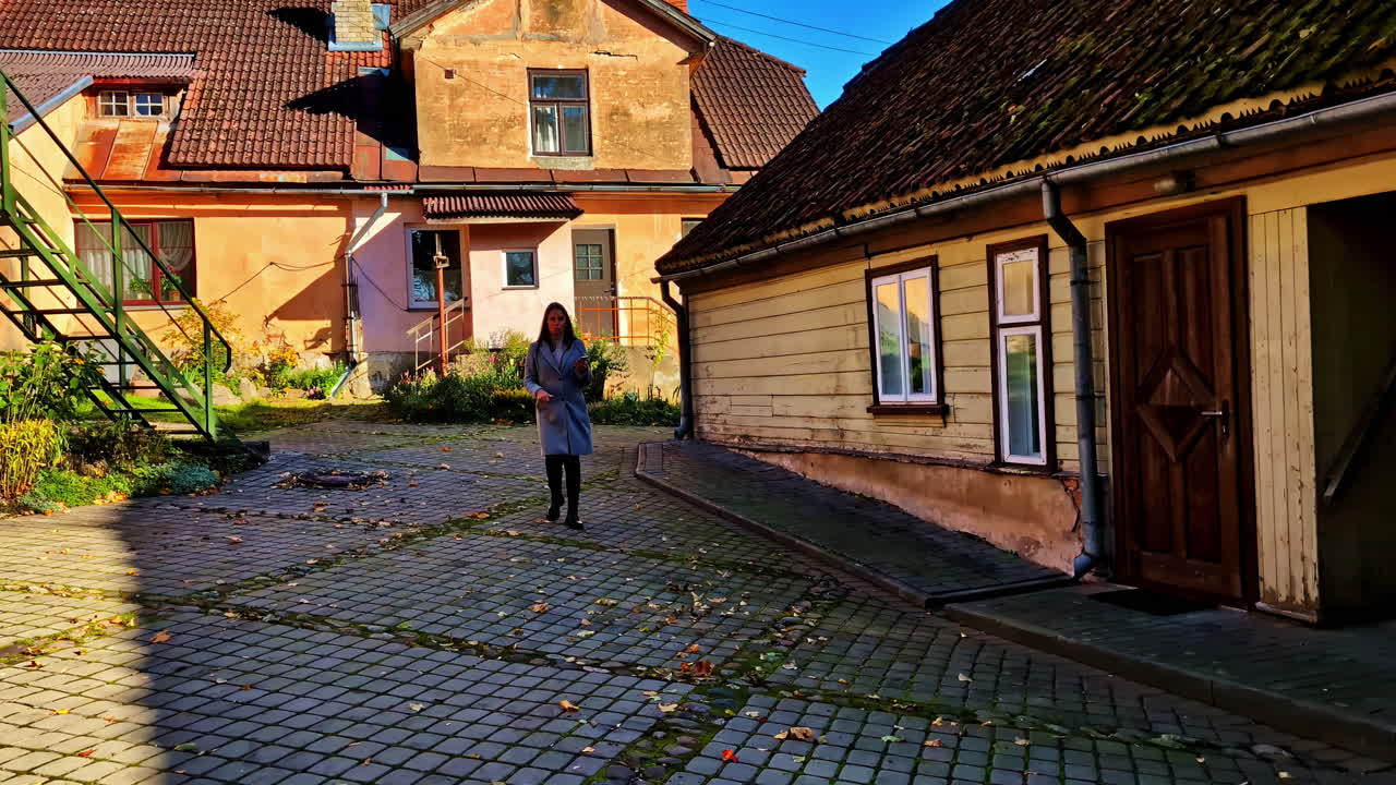 A woman walks through a quiet cobblestone courtyard surrounded by old wooden and brick homes