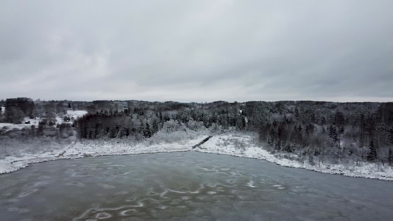 추운 겨울에 얼어붙은 호수와 어두운 숲의 공중 회전 드론 보기