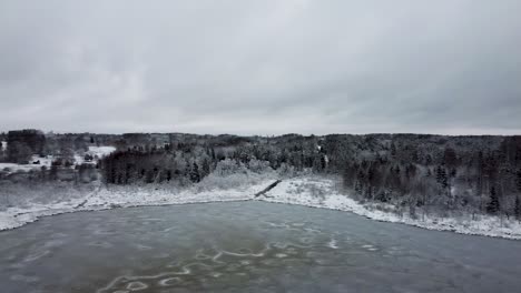 aerial rotating drone view of a frozen lake and a dark forest in cold winter