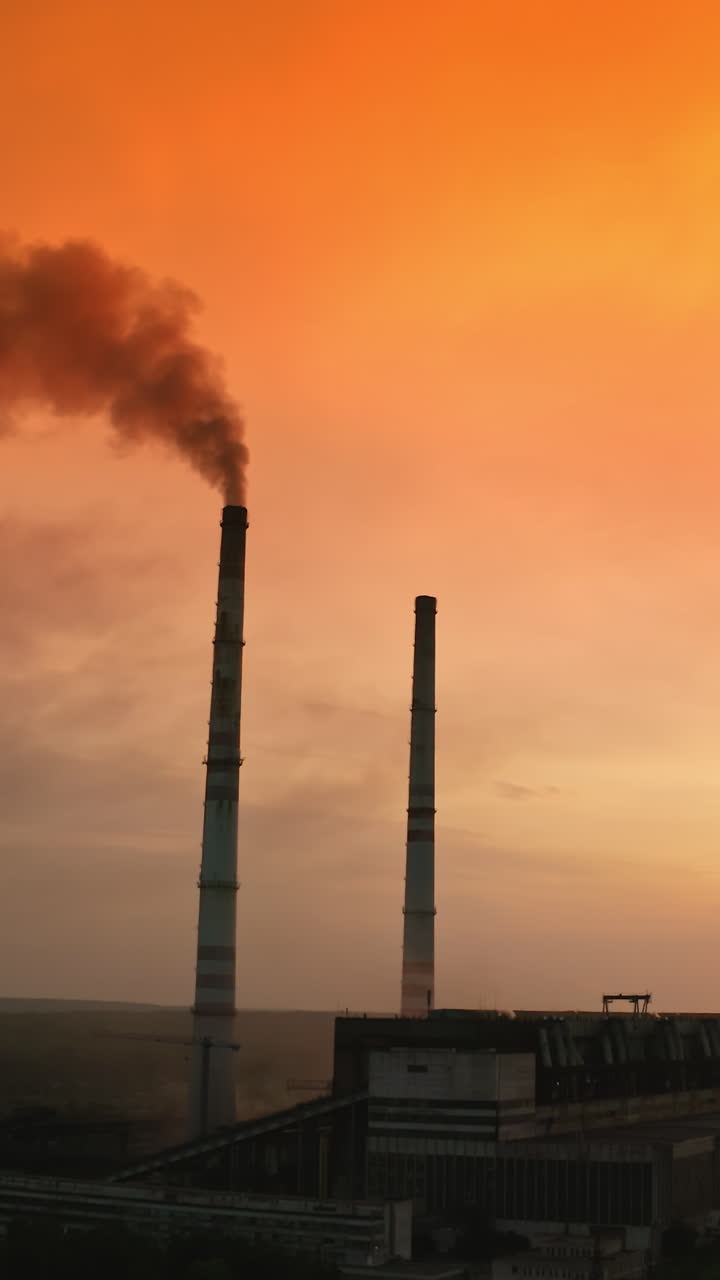 Environmental poisoning by chemical industry. Factory chimneys are blowing huge puffs of smoke into the air. Dark smoke from high pipe against background of evening nature. Vertical video