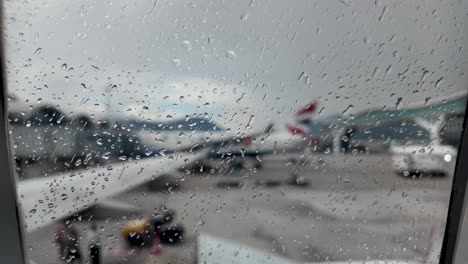 Detailed view of rain droplets on an airplane window, capturing the moody atmosphere of a rainy day at an airport.