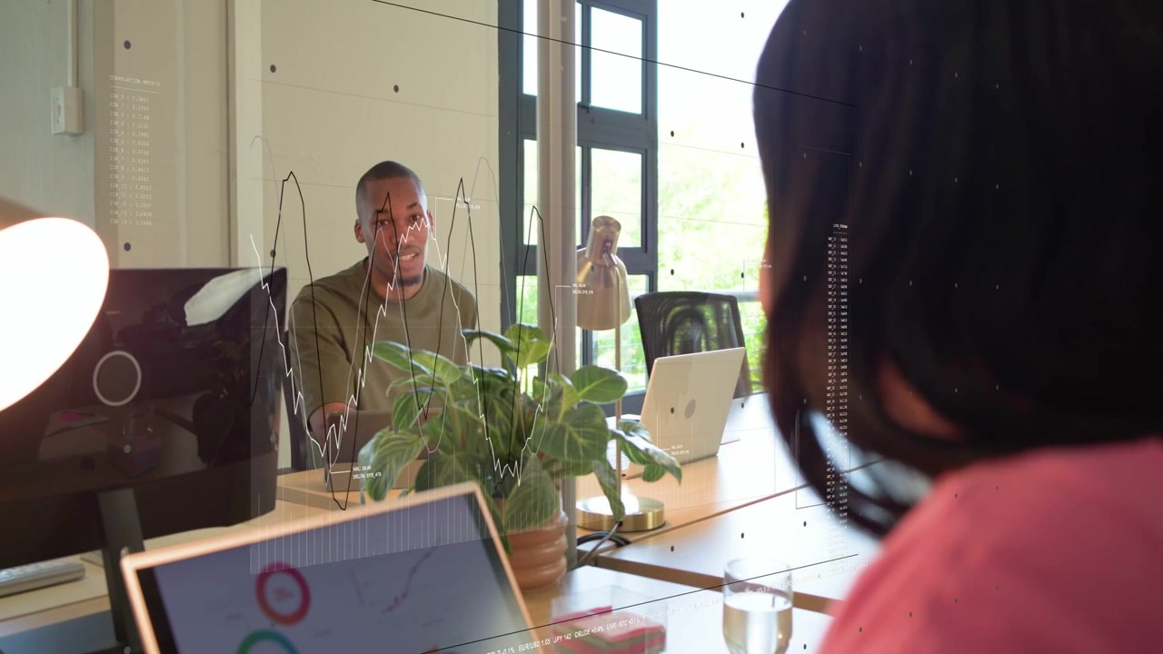 Man smiling, gesturing through glass while woman at laptop listening, charts appearing for business