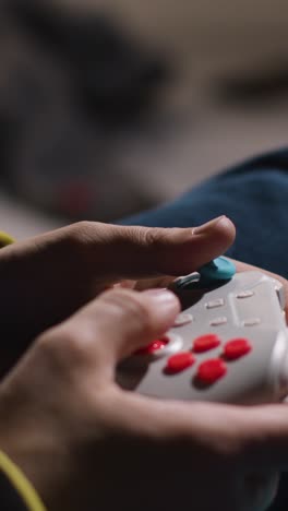 vertikal close-up-video hände mann spielt videospiel-controller sitzt sofa zu hause 2