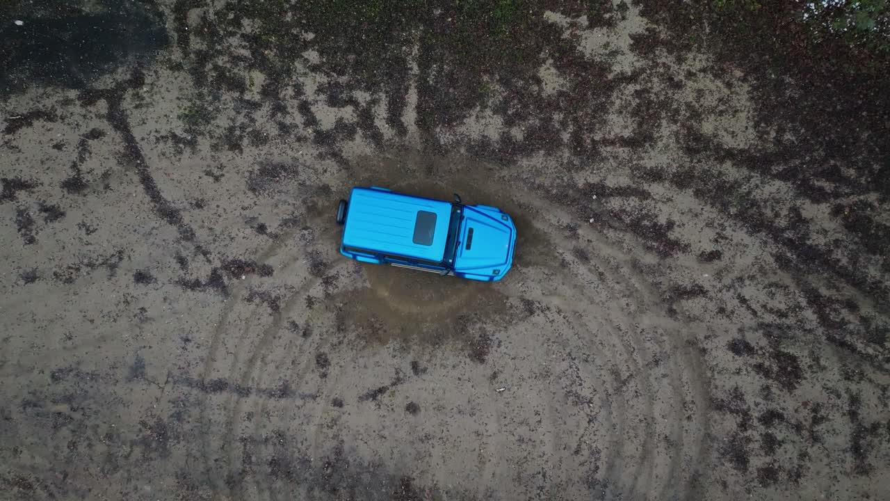 Aerial - blue off-road vehicle drive on muddy terrain track and do tank turn