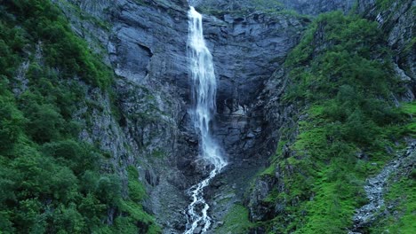 Toma-Cinematográfica-De-Drones-De-Una-Cascada-Gigantesca-Que-Salpica-Entre-Montañas-Verdes-Al-Atardecer