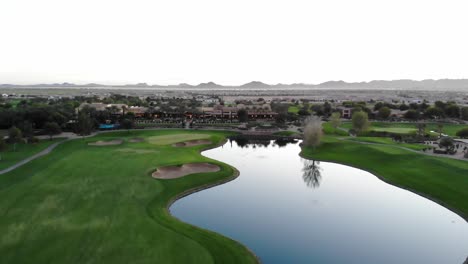 drone footage from a golf course near a residential neighborhood in arizona. high aerial shot of the greens, fairway, water harzard and clubhouse, with the arizona mountains in the background