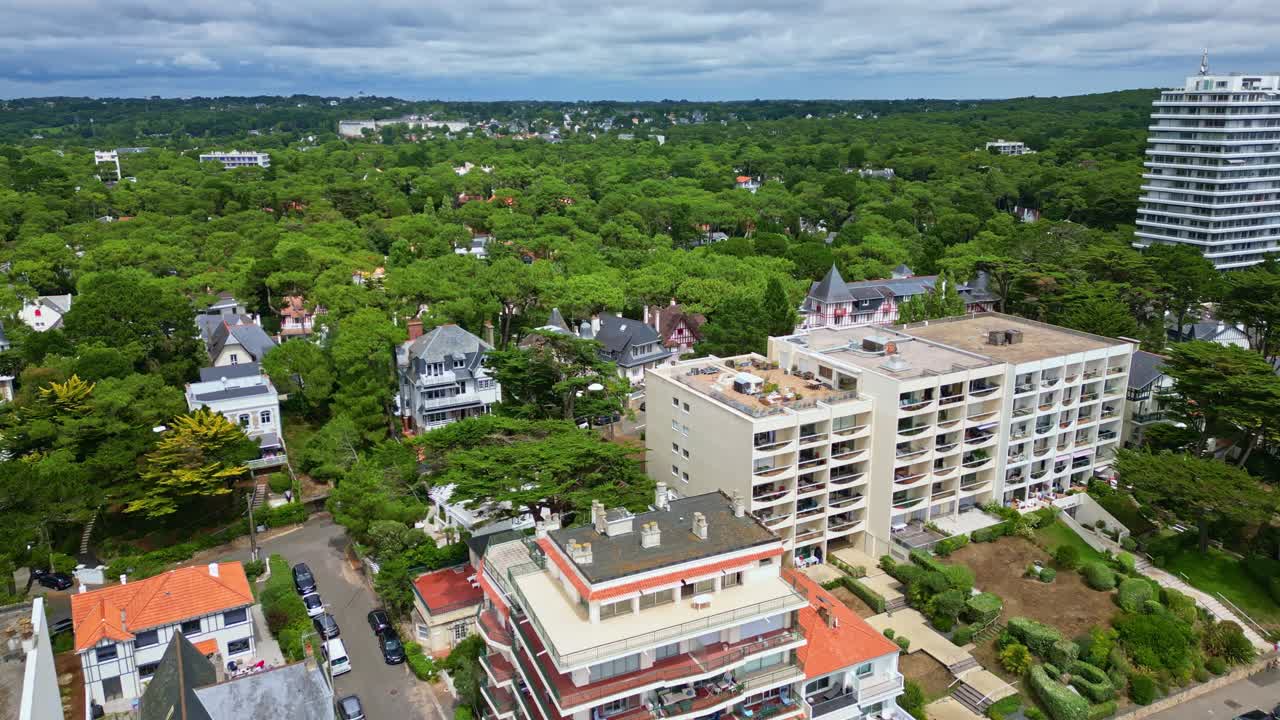 Drone descending shot from beach towards La Baule-Escoublac, showing buildings, many trees, road, and seagulls flying close to the camera