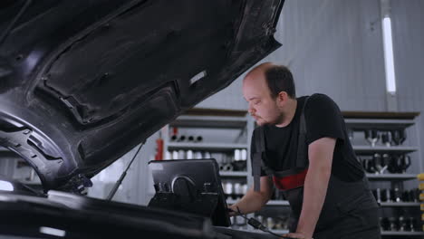 male mechanic uses a tablet computer with an augmented reality diagnostics software. specialist inspecting the car in order to find broken components inside the engine bay. modern car service.