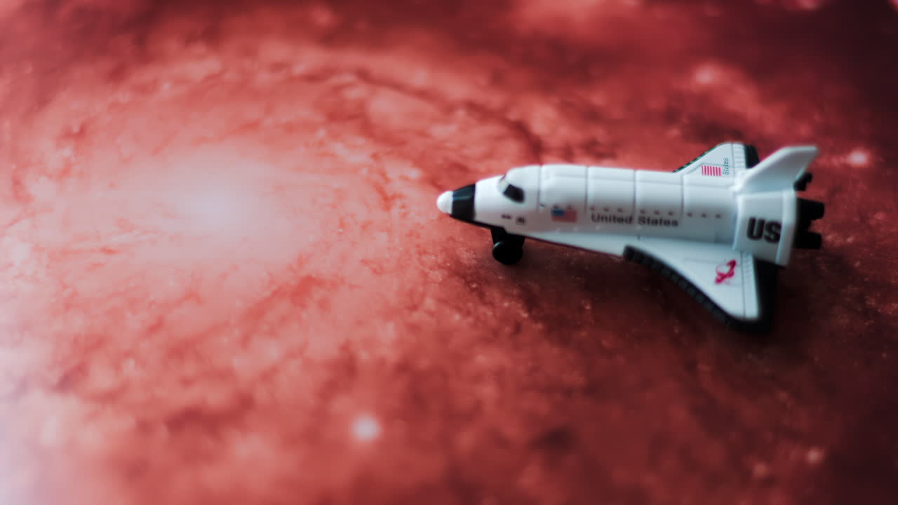 Close up of a miniature toy space shuttle placed on a reddish galaxy background