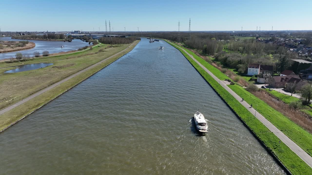 Elevating aerial view of Antwerp canal with ships sailing through waterways surrounded by fields, trees, and residential countryside areas