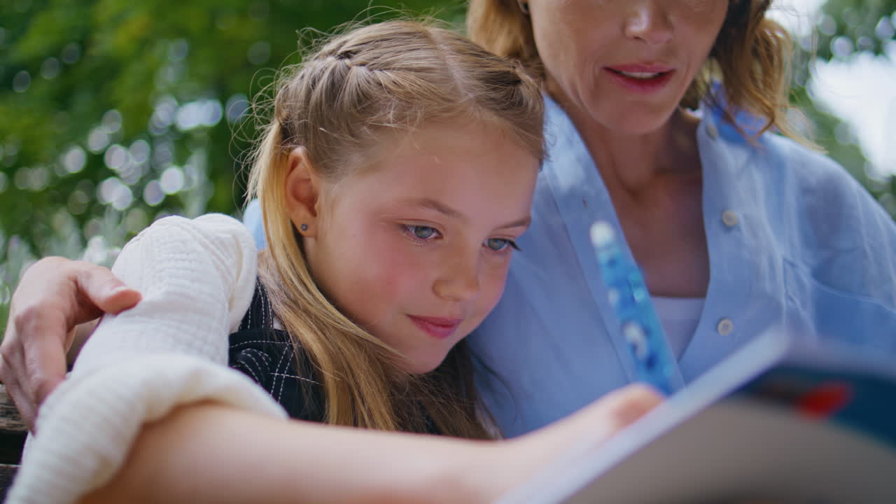 Closeup schoolgirl writing copybook doing homework with mother at greenery place