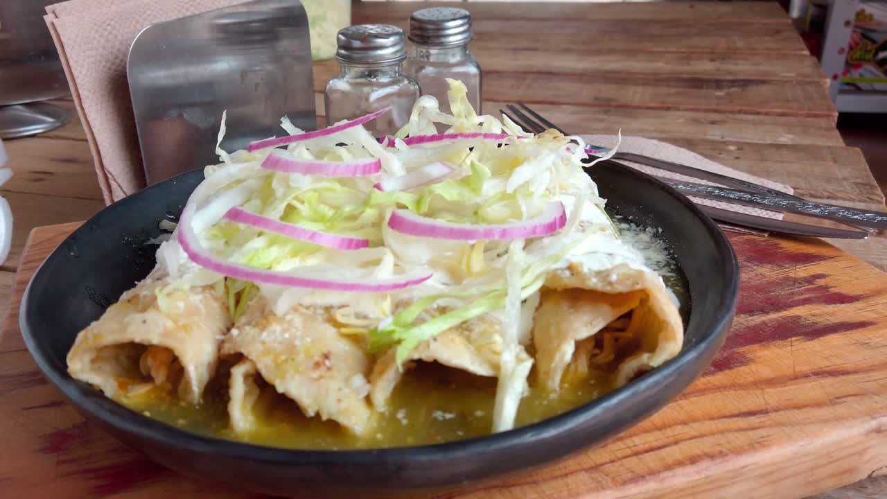 Crispy enchiladas topped with lettuce, onion, and cheese on rustic wooden table