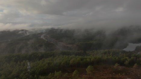 imágenes de drones de la carretera, la torre de radio y la urbanización en noruega con algo de niebla flotando en el aire y el sol iluminando las nubes