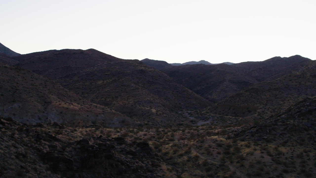 Cinematic aerial of rugged Palm Springs mountain terrain at sunrise, showcasing dramatic ridges, rocky slopes, and desert textures under a morning sky