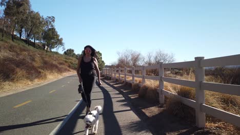 hembra hispana caminando perro maltés blanco en carril bici durante un día claro