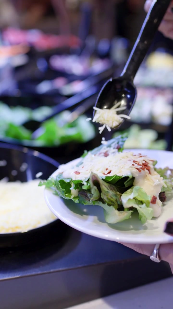 Primo piano di una mano che aggiunge formaggio a un piatto di insalata
