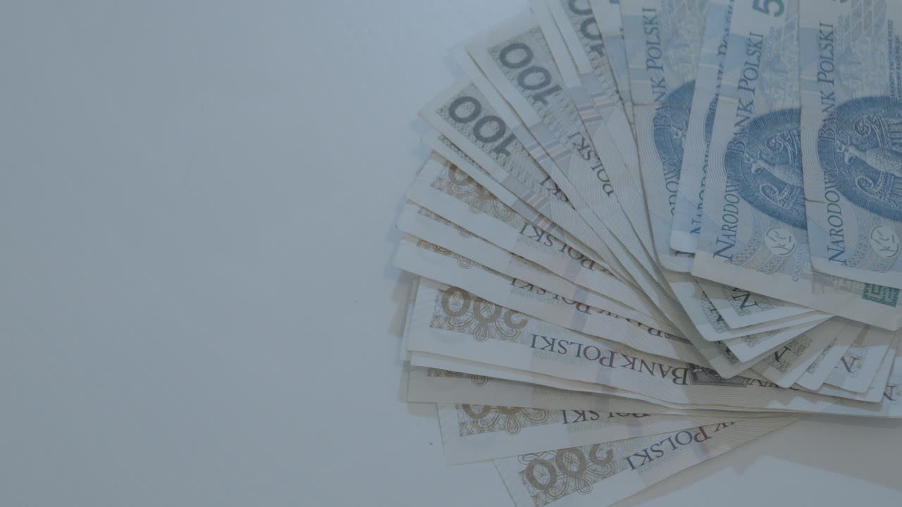 Manns hånd legger polske zloty-sedler på 50, 100 og 200 på et hvitt bord