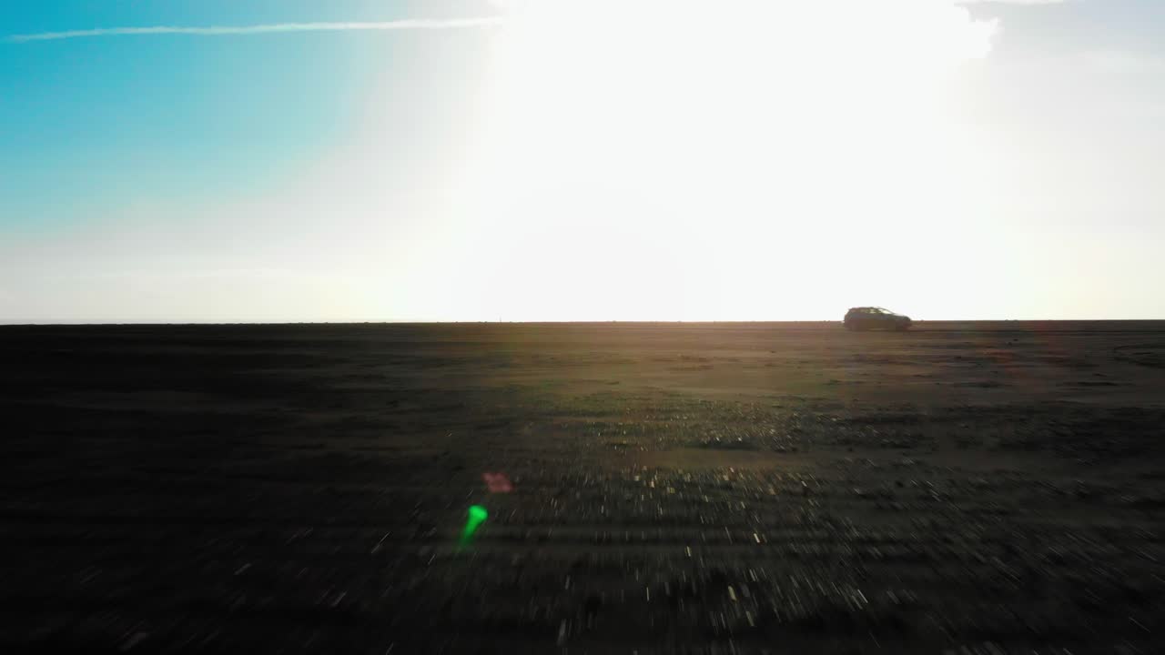 Flying towards a driving car on black beach in Iceland at sunset