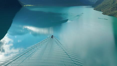 A-small-boat-moves-in-the-turquoise-waters-of-the-Loenvatnet-Lake-leaving-water-trails-and-ripples-over-the-still-mirrorlike-surface