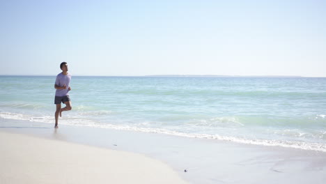 a young biracial man jogs along a sunlit beach with copy space